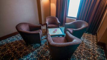 A hotel room with a patterned carpet, a small table with a vase, and two armchairs.
