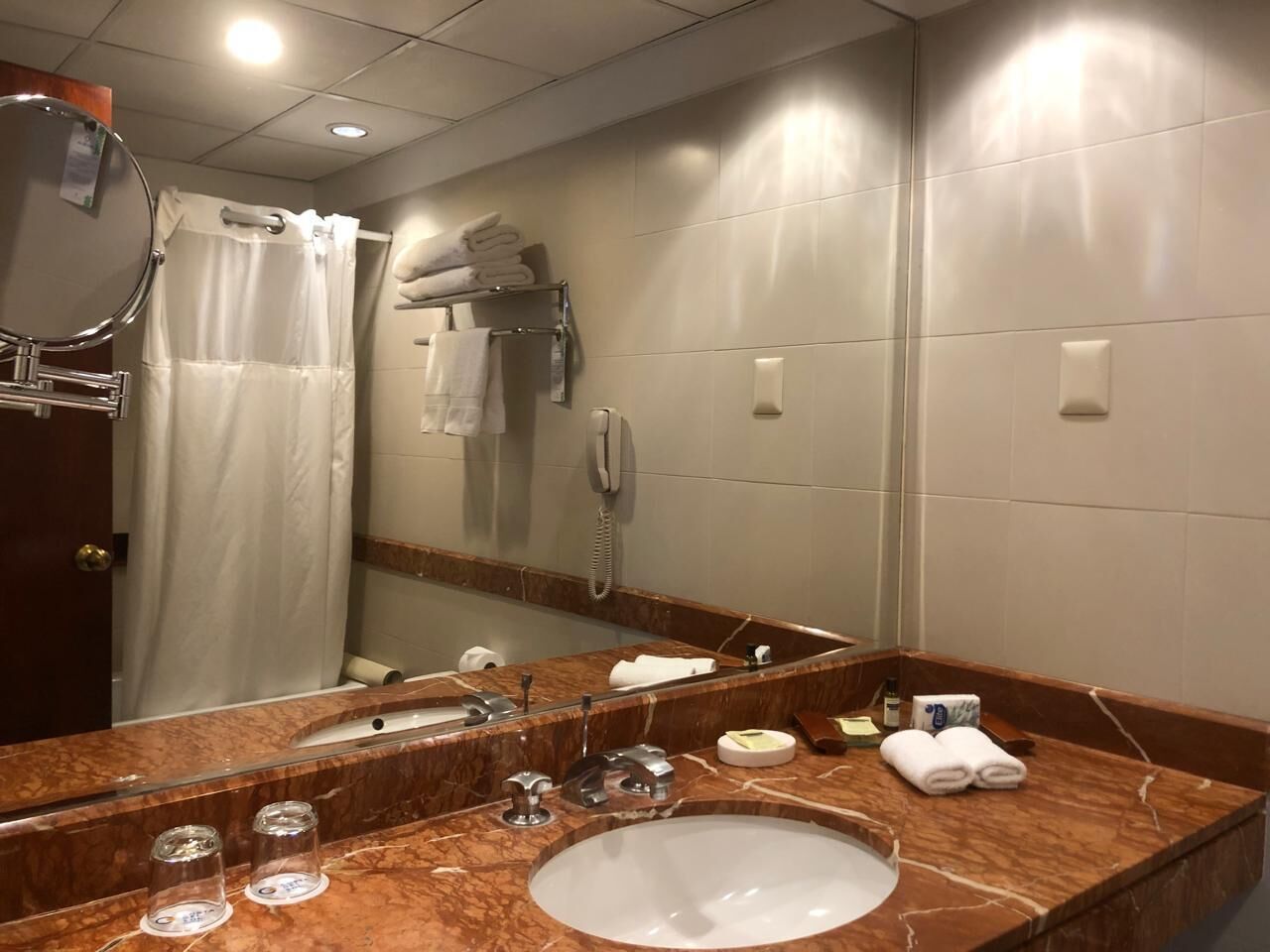 Un baño con lavamanos de mármol, un espejo grande, una cortina de ducha y un perchero para toallas.