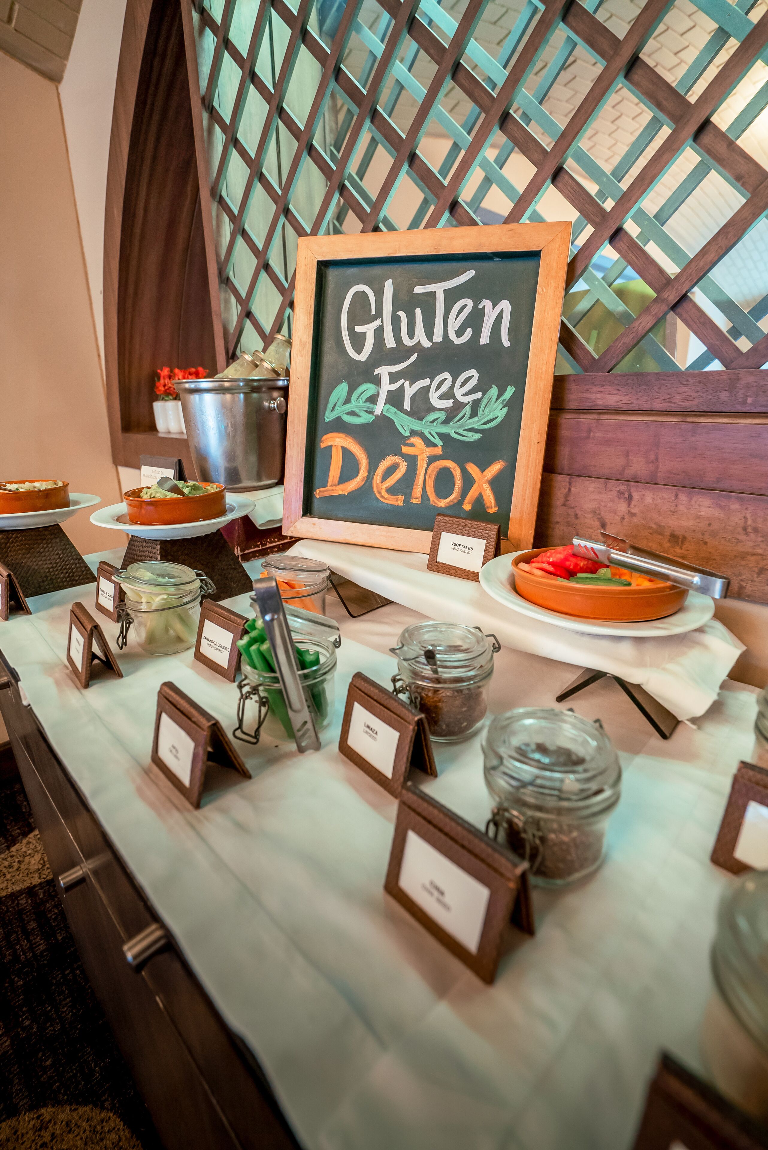 Una mesa de buffet con opciones sin gluten y desintoxicantes, varios platos y recipientes etiquetados.