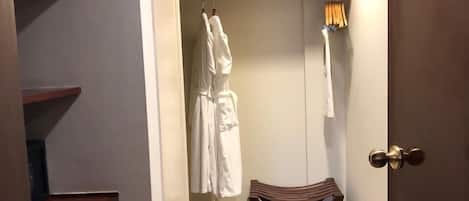 Habitación de hotel con un armario de madera, un banco y un vestidor con batas colgadas.