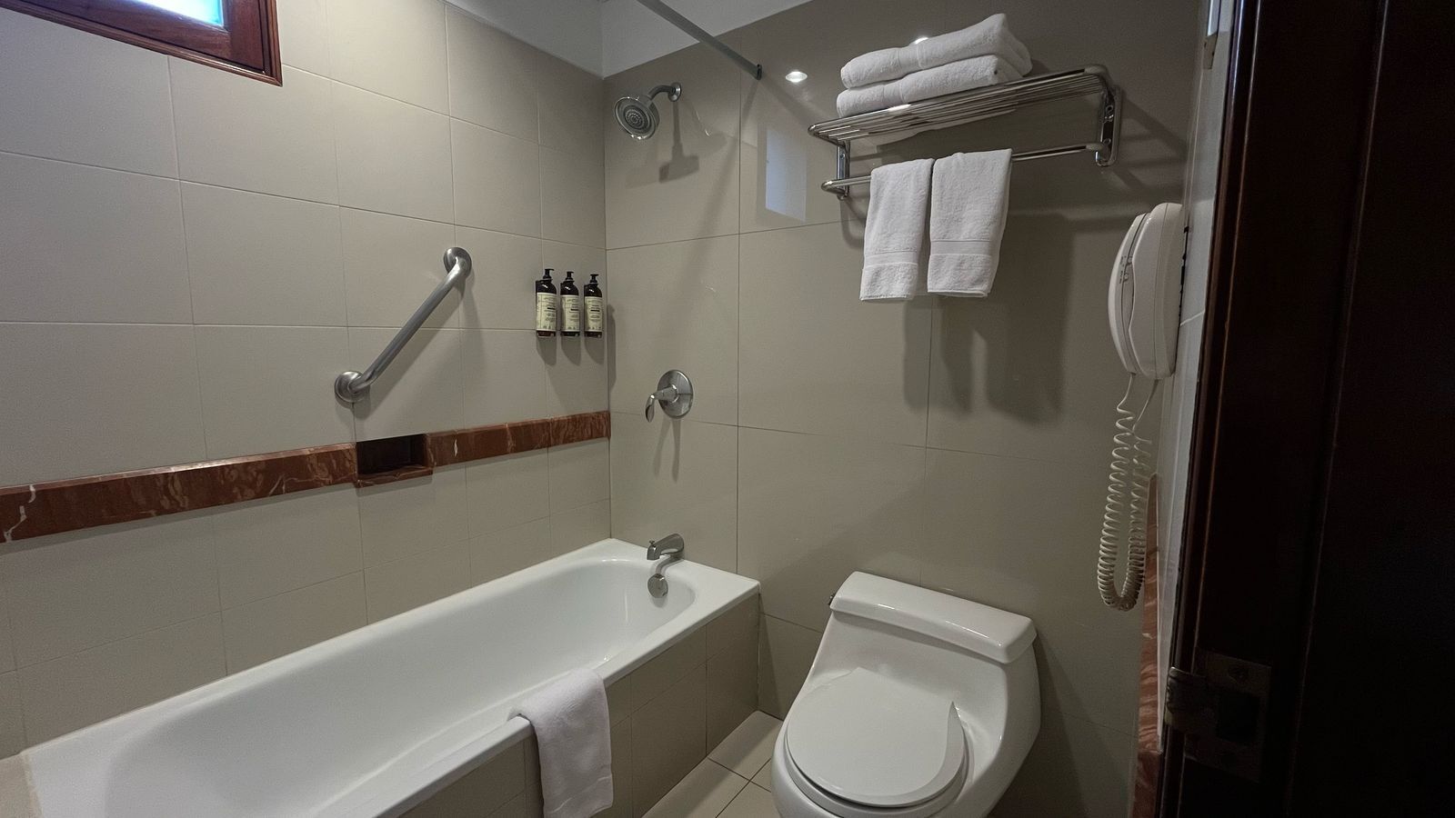 A bathroom with a bathtub, toilet, and a shower. There are towels and toiletries on the wall.