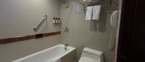 A bathroom with a bathtub, toilet, and a shower. There are towels and toiletries on the wall.