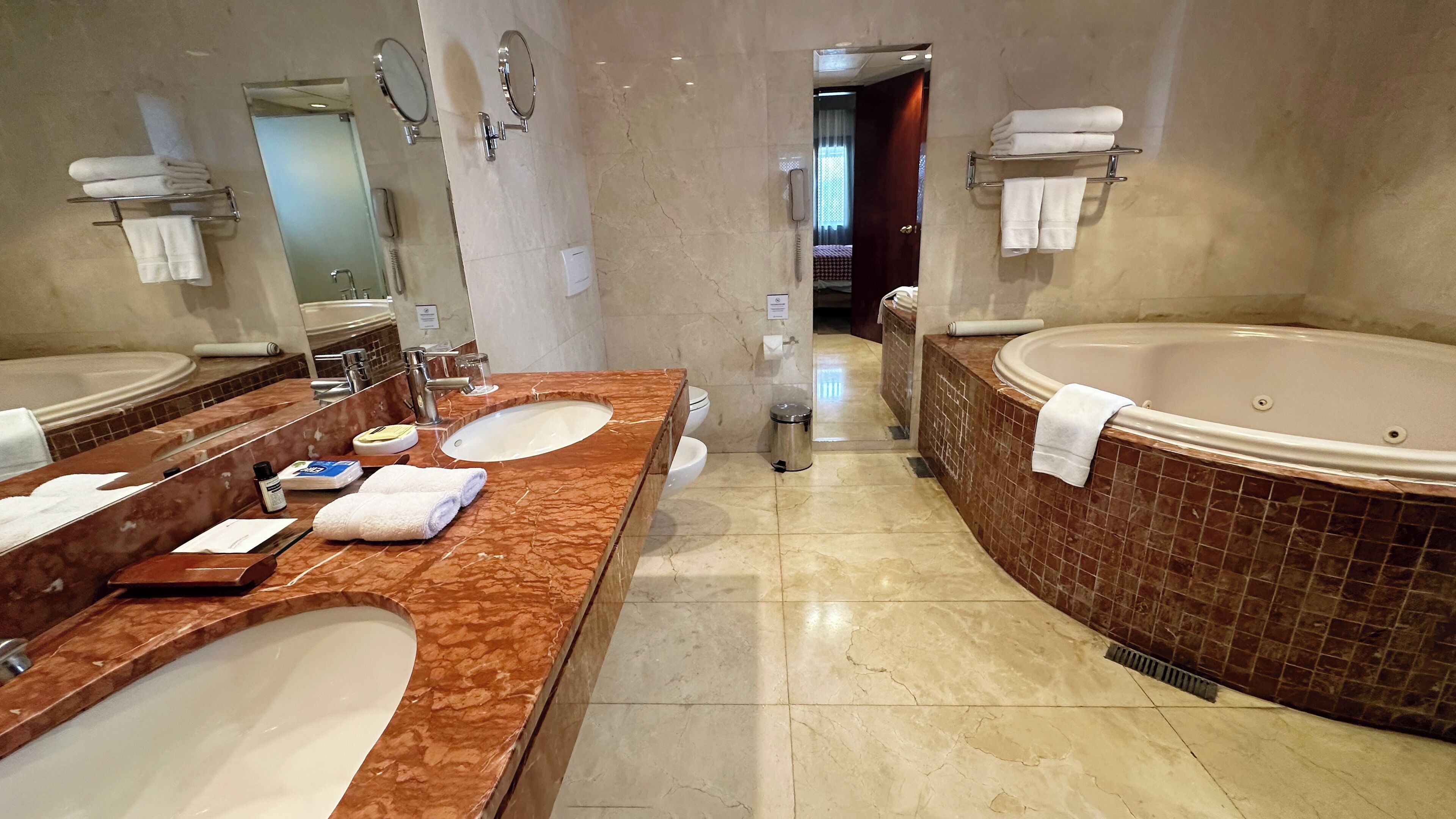 A hotel bathroom with two sinks, a bathtub, and a toilet.