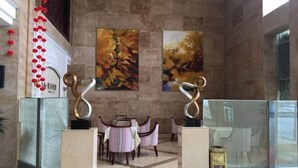 Un hall d’entrée avec un sol en marbre, des fauteuils à rayures et des œuvres d’art abstrait accrochées aux murs.