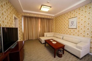 A hotel room with a sofa, a TV, a coffee table, a trash bin, and a patterned wall. - Zhijiang International Hotel (Zhijiang)