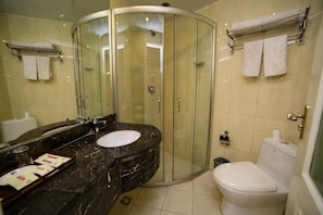 Un baño con ducha envuelta en vidrio, un lavamanos con encimera de mármol y un inodoro.
