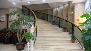 Un escalier en marbre avec des rampes en verre, des plantes en pot et des fauteuils de massage dans un espace d’accueil.