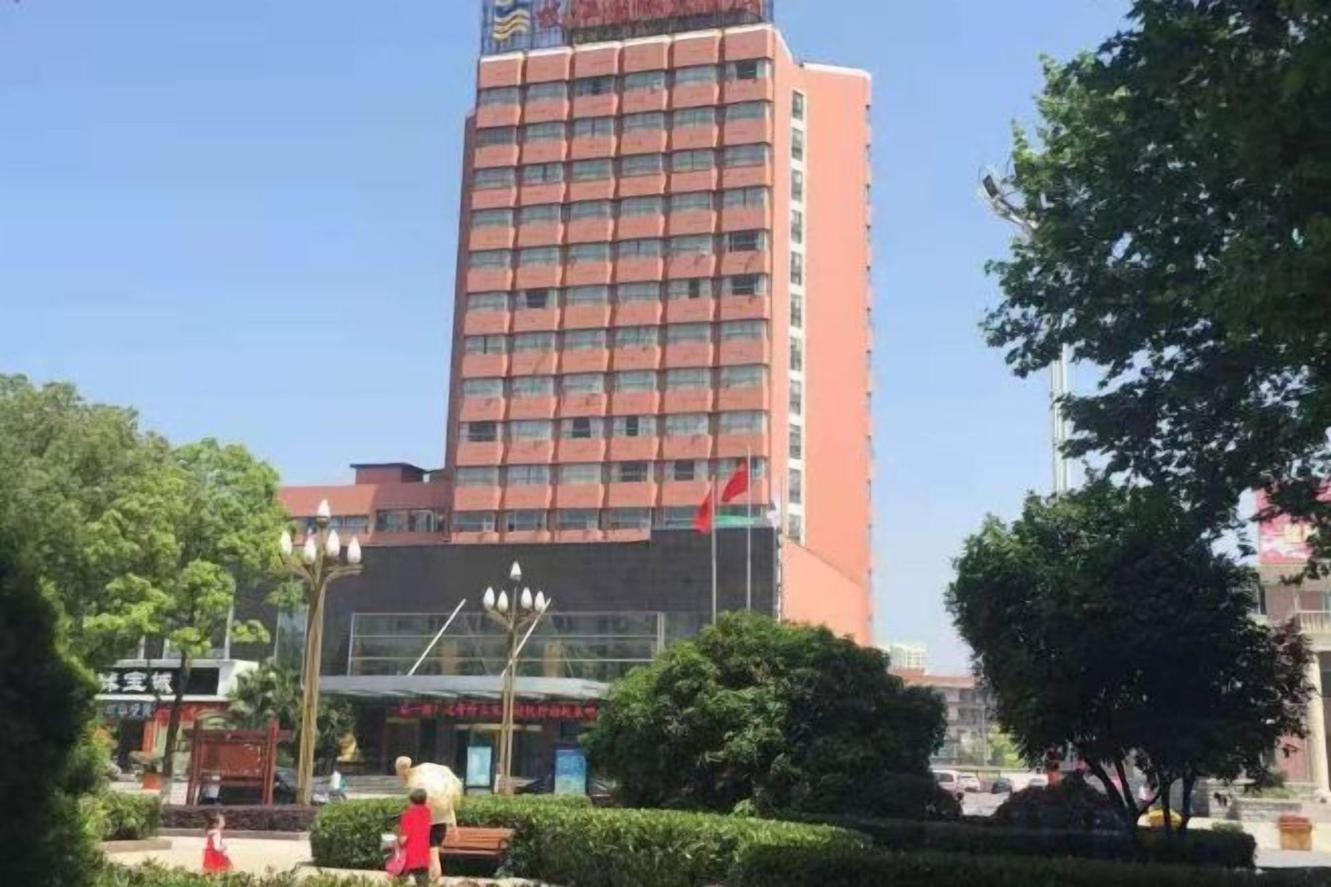 A tall building with a red facade, surrounded by greenery and a clear sky.