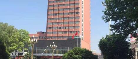 A tall building with a red facade, surrounded by greenery and a clear sky.