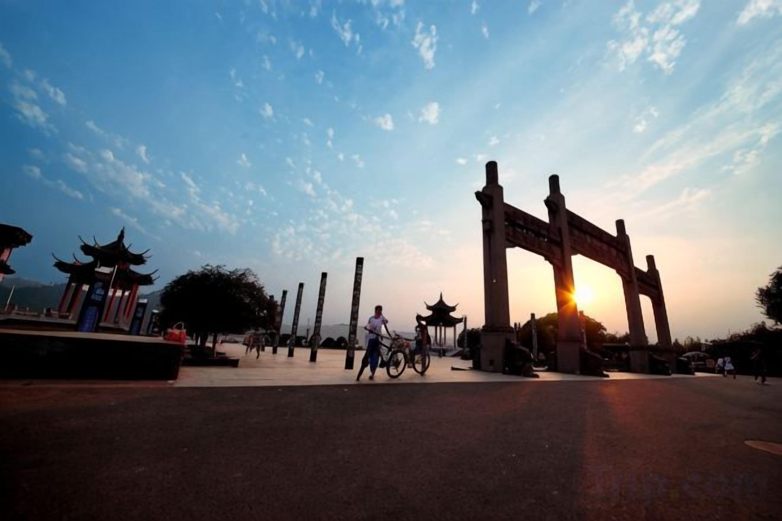 An open plaza with a large archway, a bicycle, and traditional structures.
