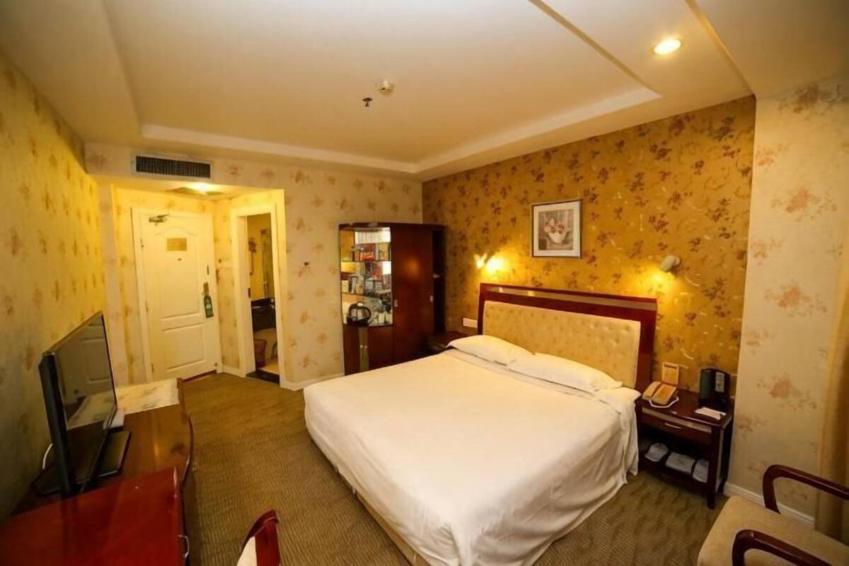 Hotelkamer met een bed, een bureau met stoel, een televisie, een kledingkast en een badkamer die door een open deur zichtbaar is.