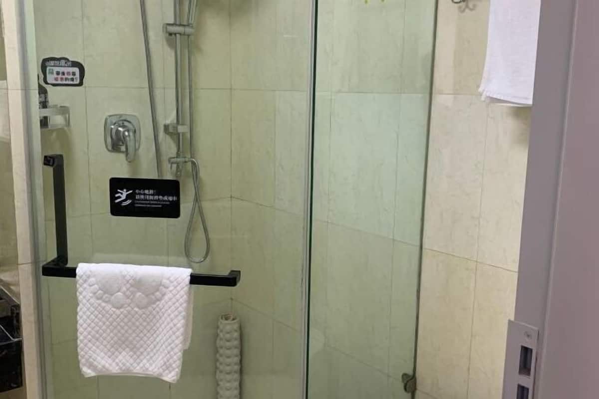 Een badkamer met een glazen scheiding, een handdoekhouder met een witte handdoek, een douchekop en een bord met Japanse tekst.