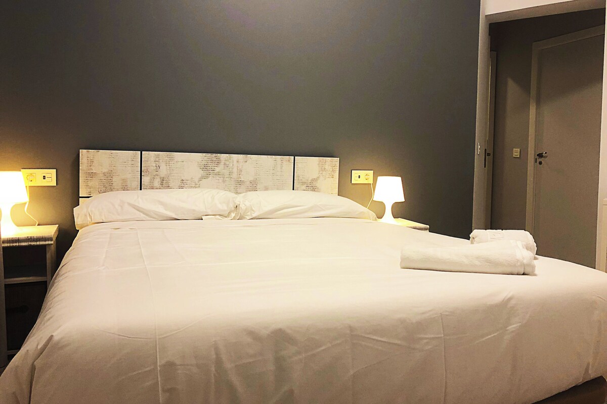 A neatly made bed with white linens, two bedside lamps, and a wall with a menu or list.