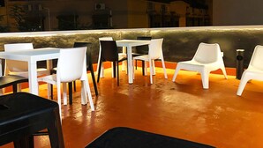 An outdoor seating area with white tables and chairs, a low wall, and a view of buildings in the background. - Butik Almería Centro (Almeria)