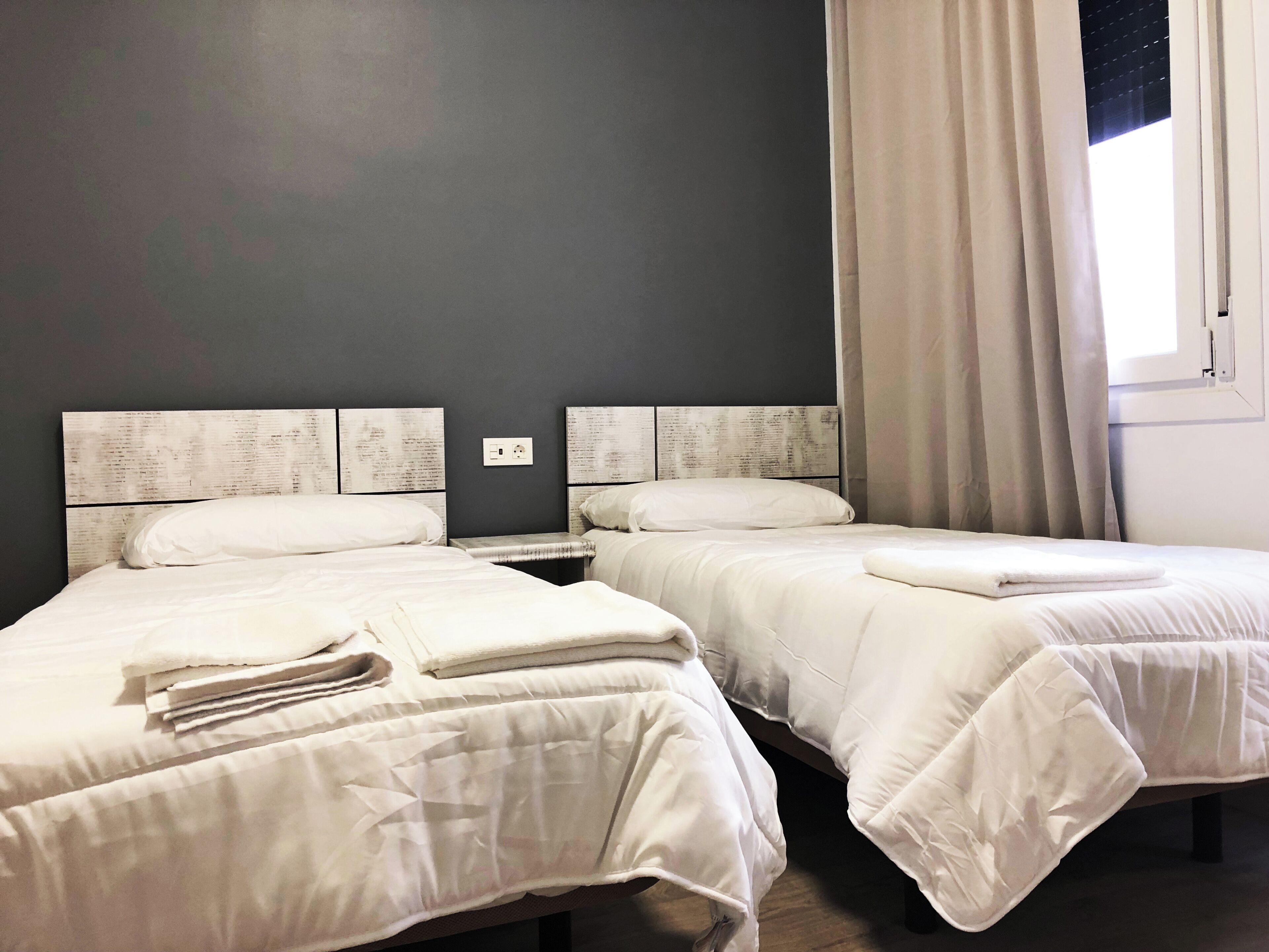 Two single beds with white bedding, a nightstand, and a wall-mounted power outlet.