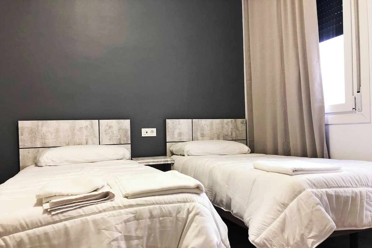 Two single beds with white bedding, a nightstand, and a wall-mounted power outlet.