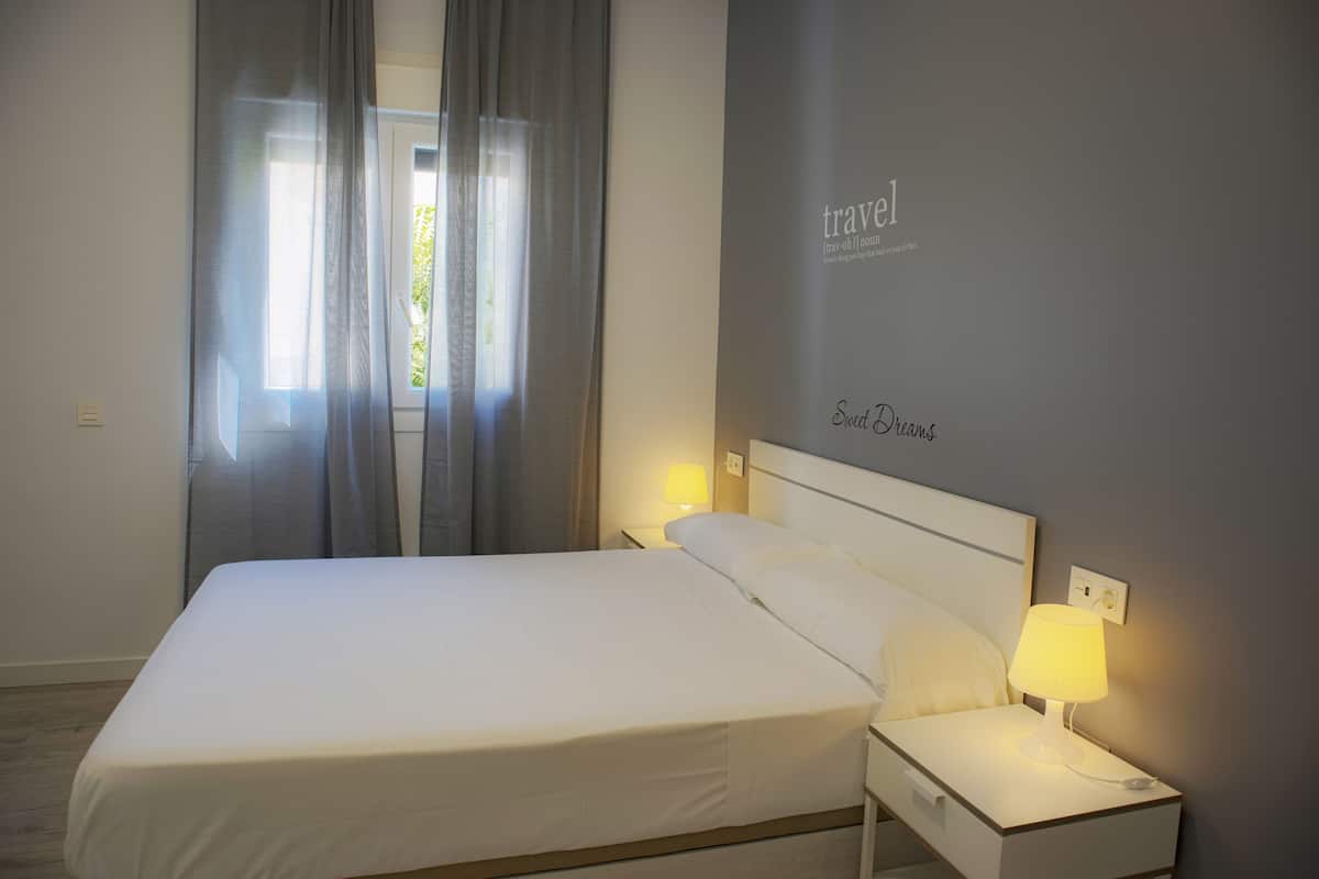 A neatly made bed with white linens, a bedside lamp, and a wall with the words "travel" and "Sweet Dreams".