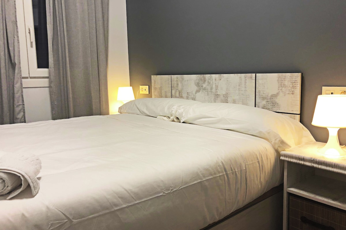 A neatly made bed with white linens, two bedside lamps, and a wall with a decorative panel.