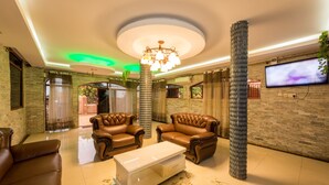 A spacious lobby with leather sofas, a white coffee table, a decorative pillar, and a television on the wall. - Chocolate Luxury Hotel (Kampala)