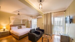 A hotel room with a bed, two armchairs, a glass table, a TV, and a ceiling light. - Chocolate Luxury Hotel (Kampala)