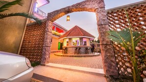 A building with a stone archway entrance, a small patio area with chairs, and a red-roofed structure. - Chocolate Luxury Hotel (Kampala)