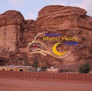 A large rock formation with a campsite and a logo for Moon Valley Camp. - Moon Valley Camp (Wadi Rum)