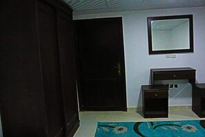 A room with a closed door, a small desk with drawers, a mirror on the wall, and a blue patterned rug on the floor. - Moon Valley Camp (Wadi Rum)