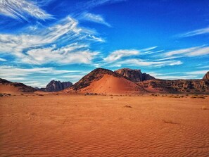 A desert landscape with sand dunes and rocky formations under a clear sky. - Moon Valley Camp (Wadi Rum)