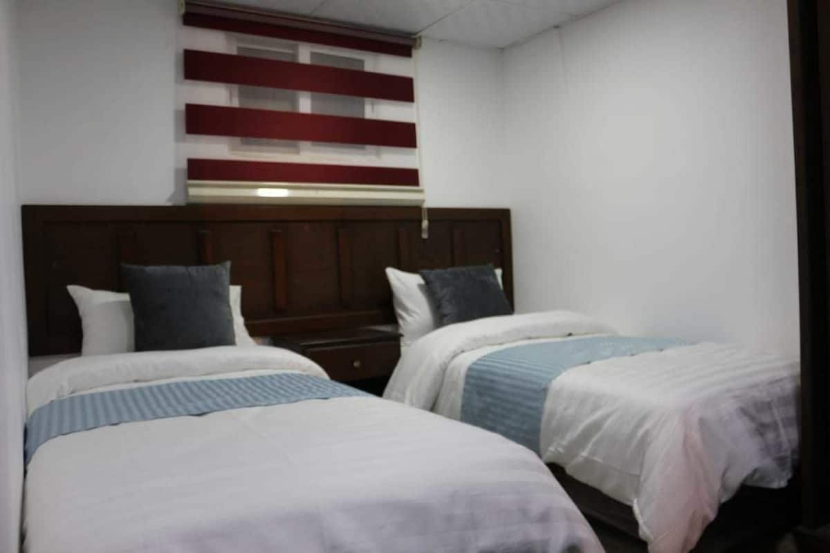 A hotel room with two single beds, a wooden headboard, and a red and white striped wall decoration.
