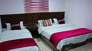 A hotel room with two beds, each with white bedding and red accents. There is a wooden headboard, a nightstand, and a window with blinds. - Moon Valley Camp (Wadi Rum)