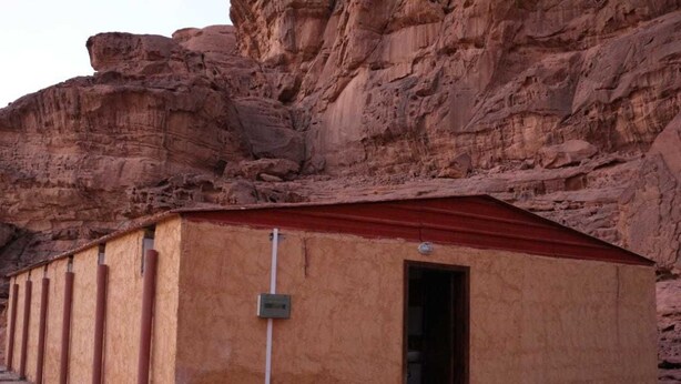 A building with a red roof and beige walls, situated against a rocky cliff. - Moon Valley Camp (Wadi Rum)