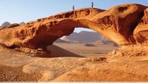 A natural rock arch formation with two people standing on top. - Moon Valley Camp (Wadi Rum)