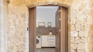 Ein Eingang zu einem Steinhaus mit Ziegeldach, der in einen Küchenbereich mit Waschmaschine und Schränken führt.
