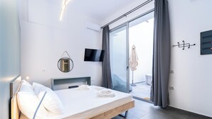 Ein modernes Schlafzimmer mit einem Bett, einem Flachbildfernseher, einem Spiegel und einer Glastür zum Balkon.