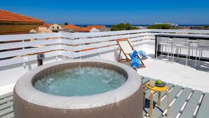 Eine Dachterrasse mit Whirlpool, Sitzgelegenheiten und Blick auf das Meer.
