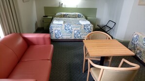Habitación de hotel con sofá rojo, mesa de madera con dos sillas, cama con diseño y un pequeño escritorio con silla.