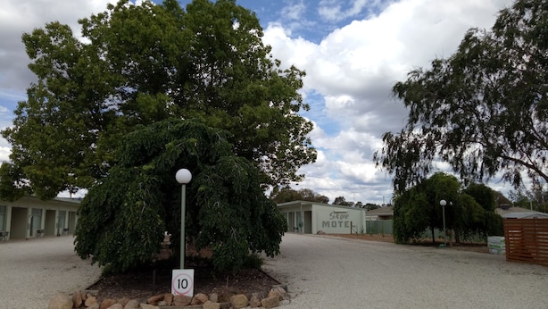 Un motel con un árbol grande al frente, una señal de límite de velocidad y un cielo despejado.