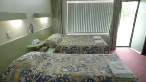Una habitación de hotel con dos camas, una mesita de noche con teléfono y una ventana con persianas.