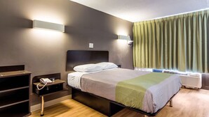 A hotel room with a bed, bedside table, lamp, and a window with curtains.