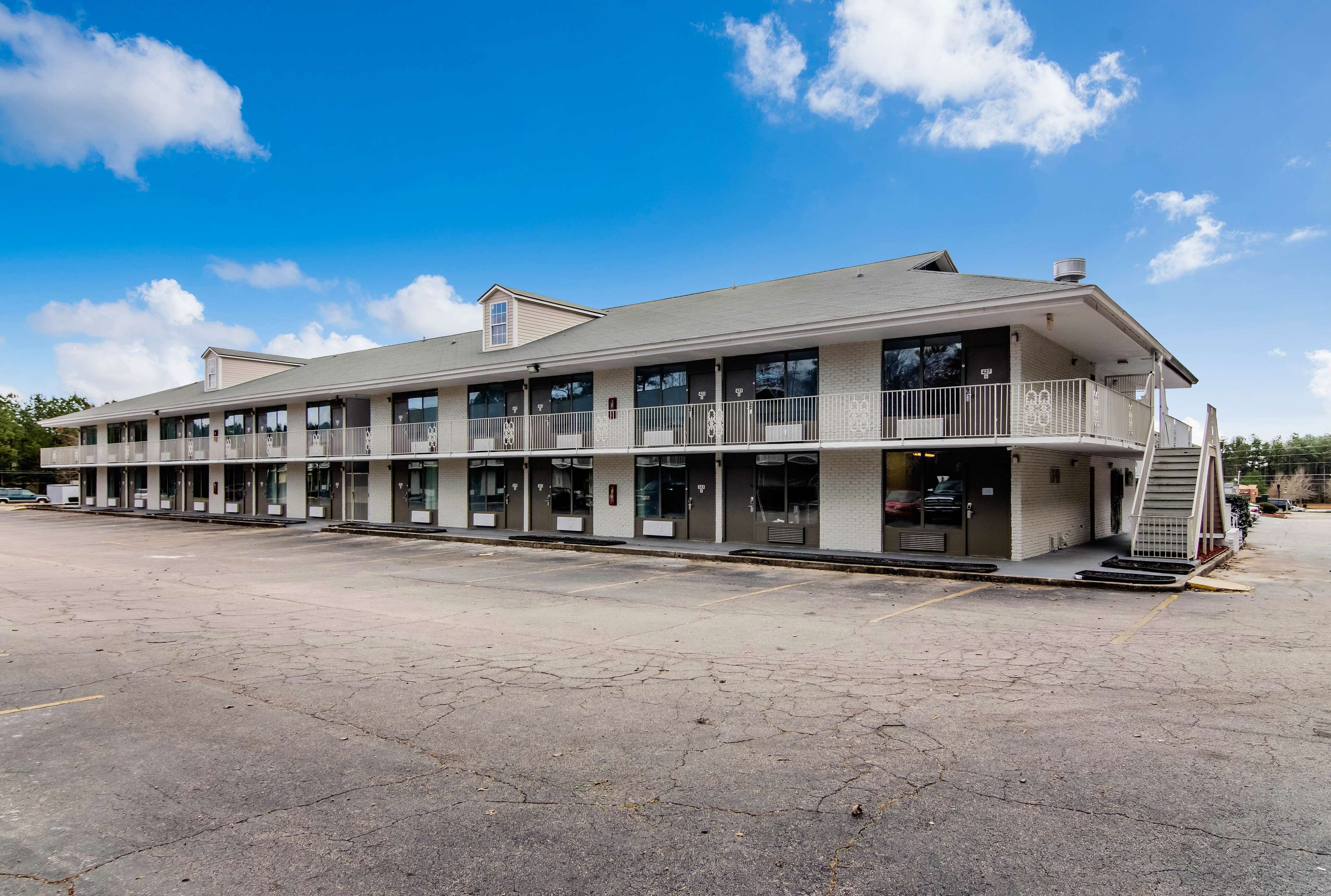 Un motel de dos pisos con techo plano, varios balcones y un estacionamiento al frente.