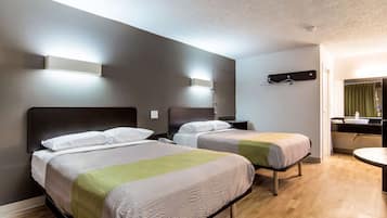 Ein Hotelzimmer mit zwei Betten, einem kleinen Nachttisch, einer Wandleuchte, einem Spiegel und einem Badezimmer mit Waschbecken und Spiegel.