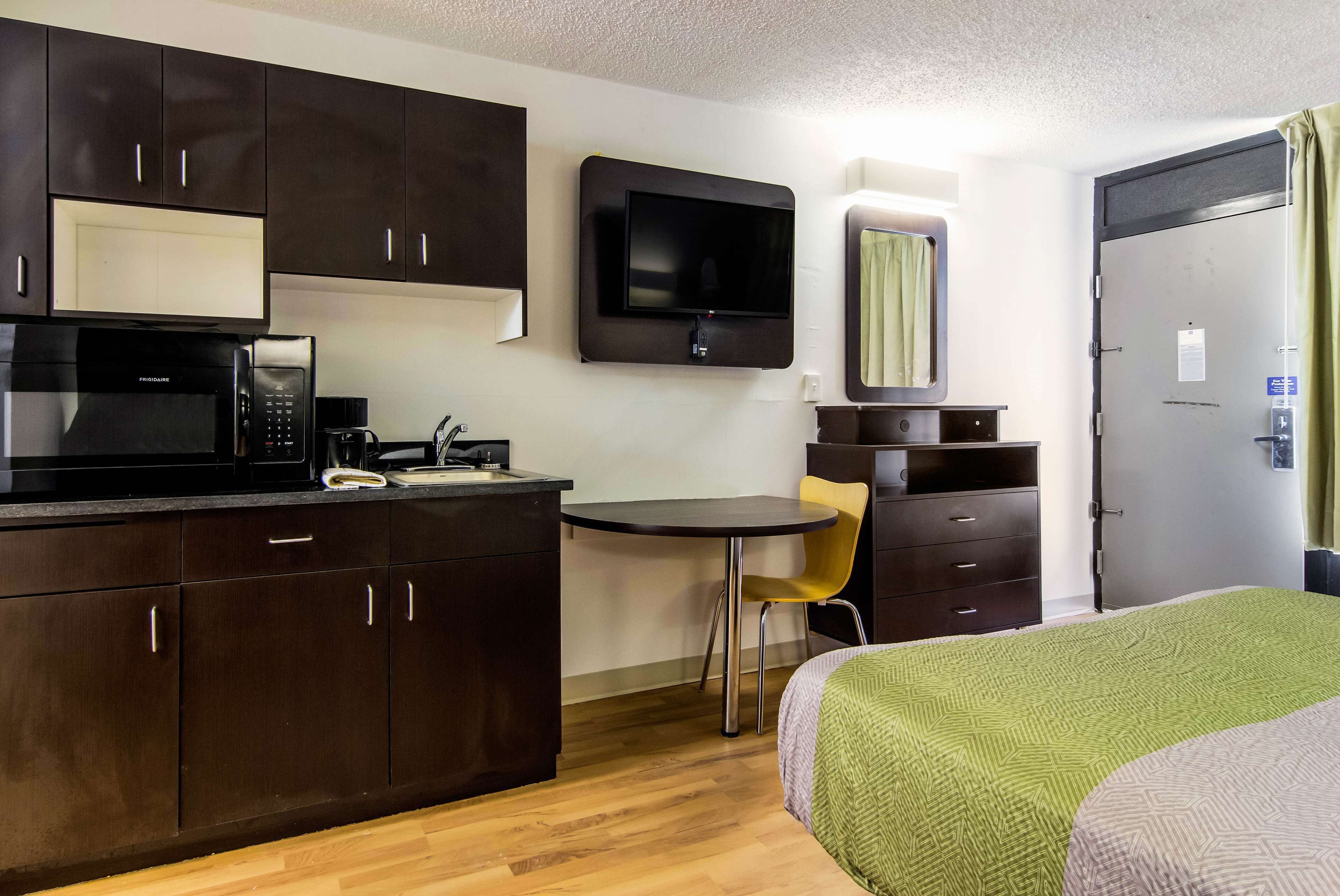 Una habitación de hotel compacta con kitchenette, una cama, un televisor y una pequeña mesa con una silla.