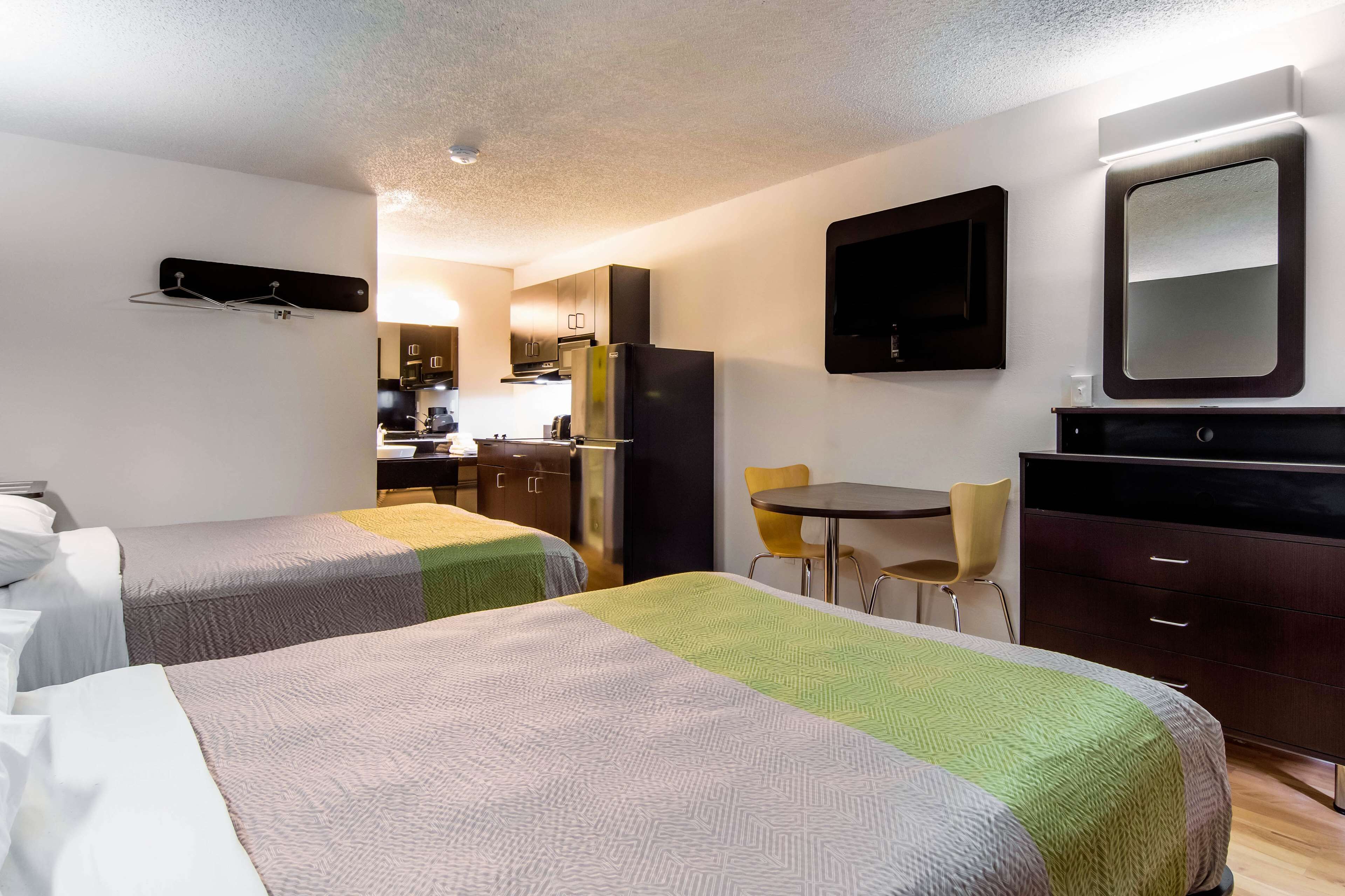 Een hotelkamer met twee bedden, een kleine keuken, een eettafel en een spiegel.