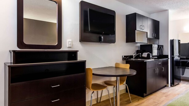 Una cocina compacta con estufa integrada, microondas y refrigerador. Hay un pequeño comedor con una mesa y dos sillas.