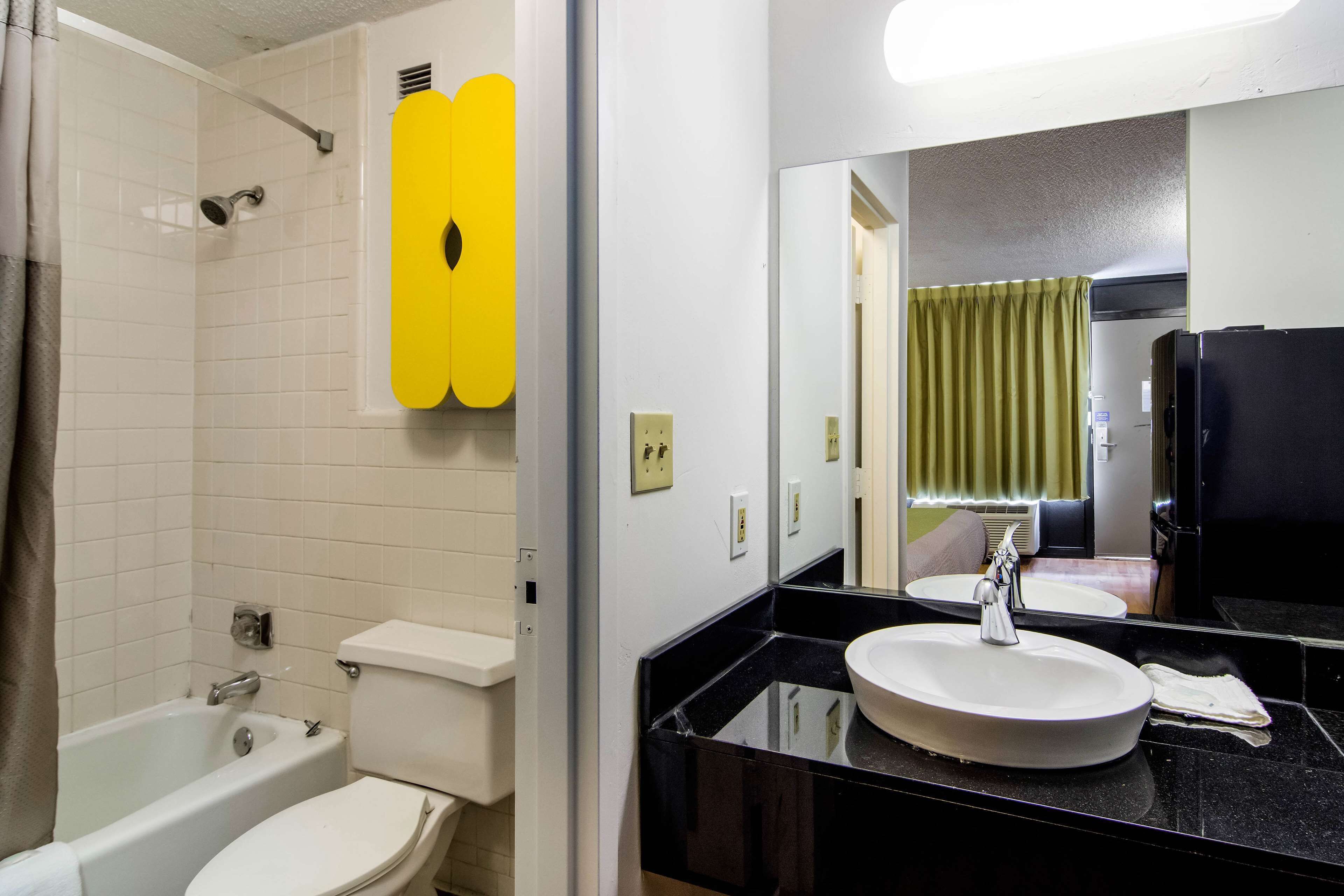 Een badkamer met een wit toilet, een badkuip, een wastafel met spiegel en een geel accentmuur.