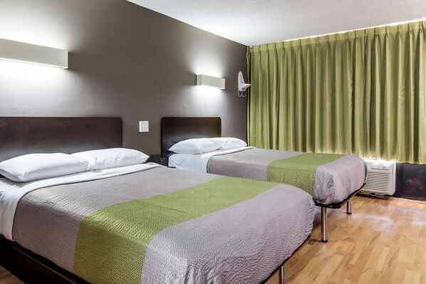 Una habitación de hotel con dos camas, cada una con cabecero, mesita de noche y lámpara. El suelo es de madera y las cortinas son verdes.