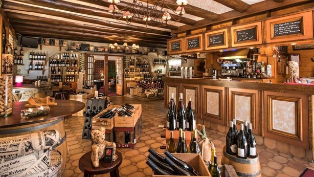 A bar with wooden beams, a chandelier, and a variety of wine bottles and glasses.