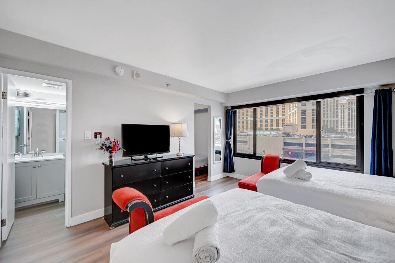 A hotel room with two beds, a TV, a dresser, and a window with a city view.