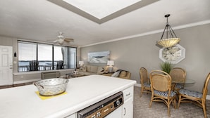 Une cuisine moderne dotée d’un grand îlot central, d’un coin repas avec des chaises en osier et d’un ventilateur de plafond.