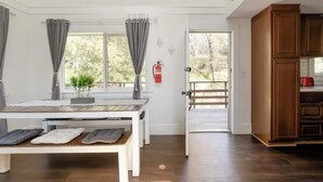A room with a wooden dining table, grey curtains, a fire extinguisher, and a view of trees through a door. - Cozy Treetop A-Frame, Fireplace, Arcade Games, Record Player (Lake Arrowhead)